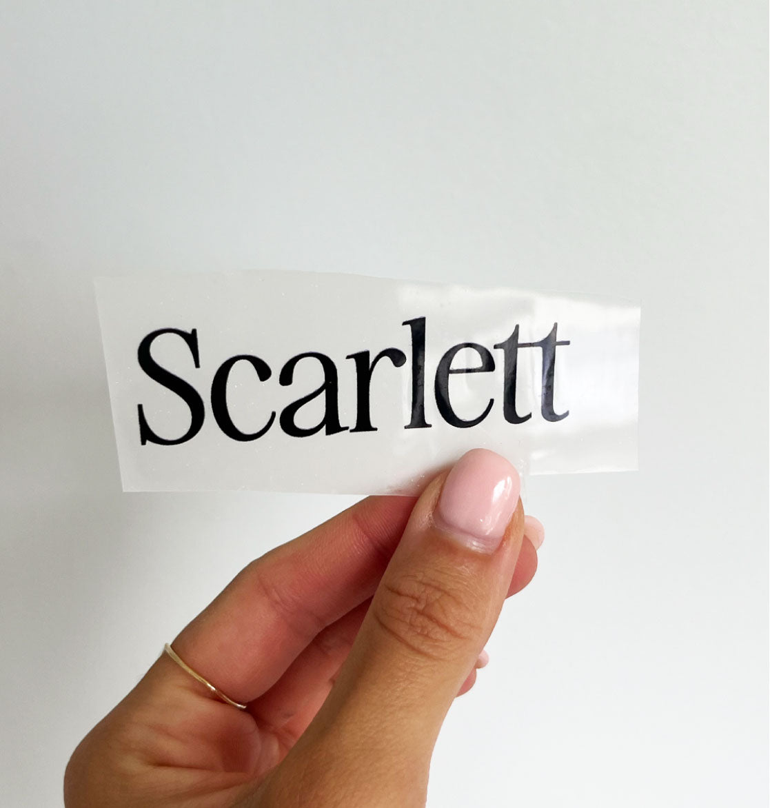 Hand holding up a DTF transfer film that says "Scarlett" 