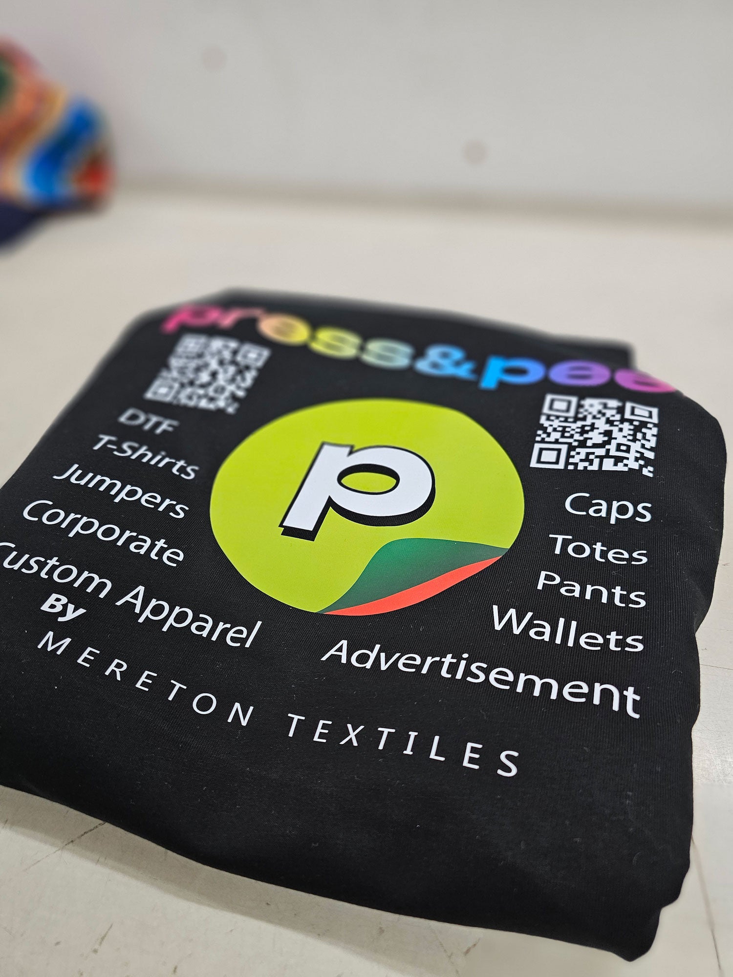 A folded black shirt that has the Press&Peel logo on it