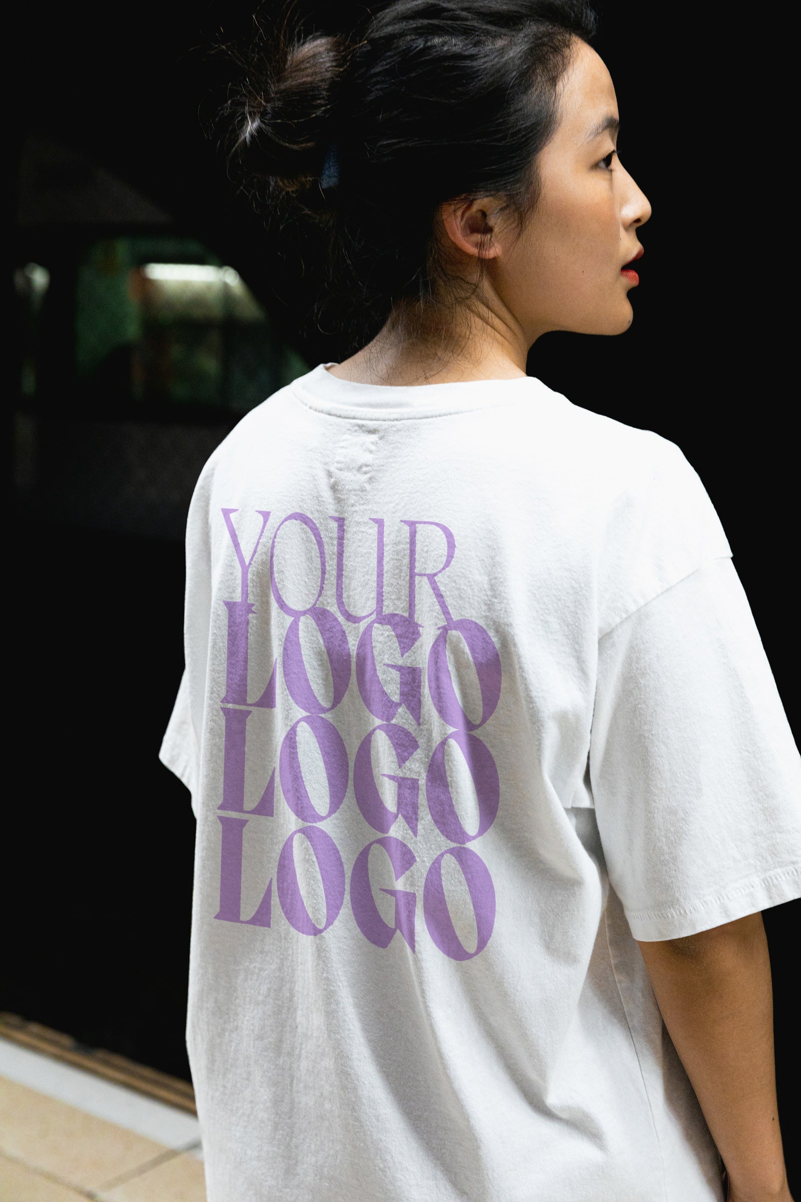 Woman facing away from the camera with a white shirt on it that says "your logo here"